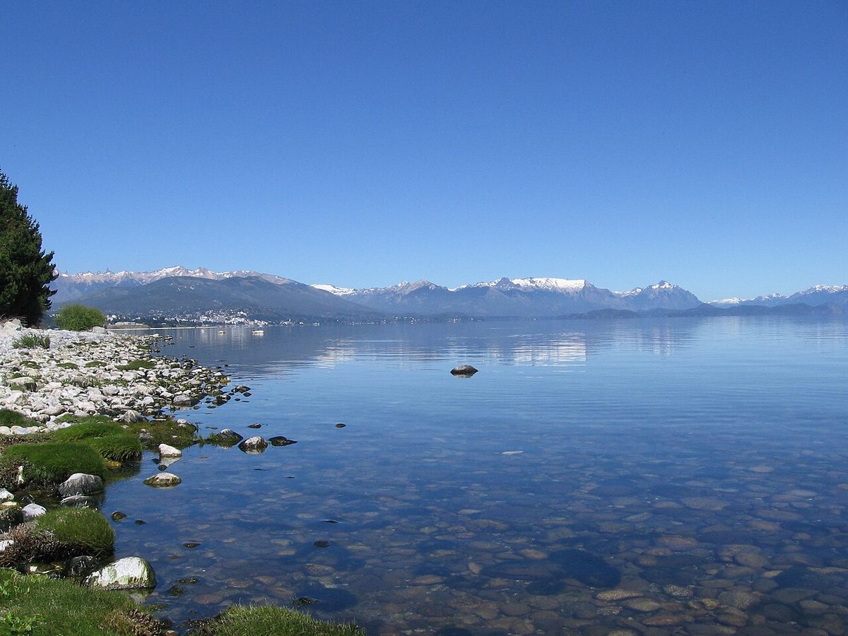 Clear water and a stony shore on Lake Nahuel Huapi near Bariloche, with snow on the mountains across the lake