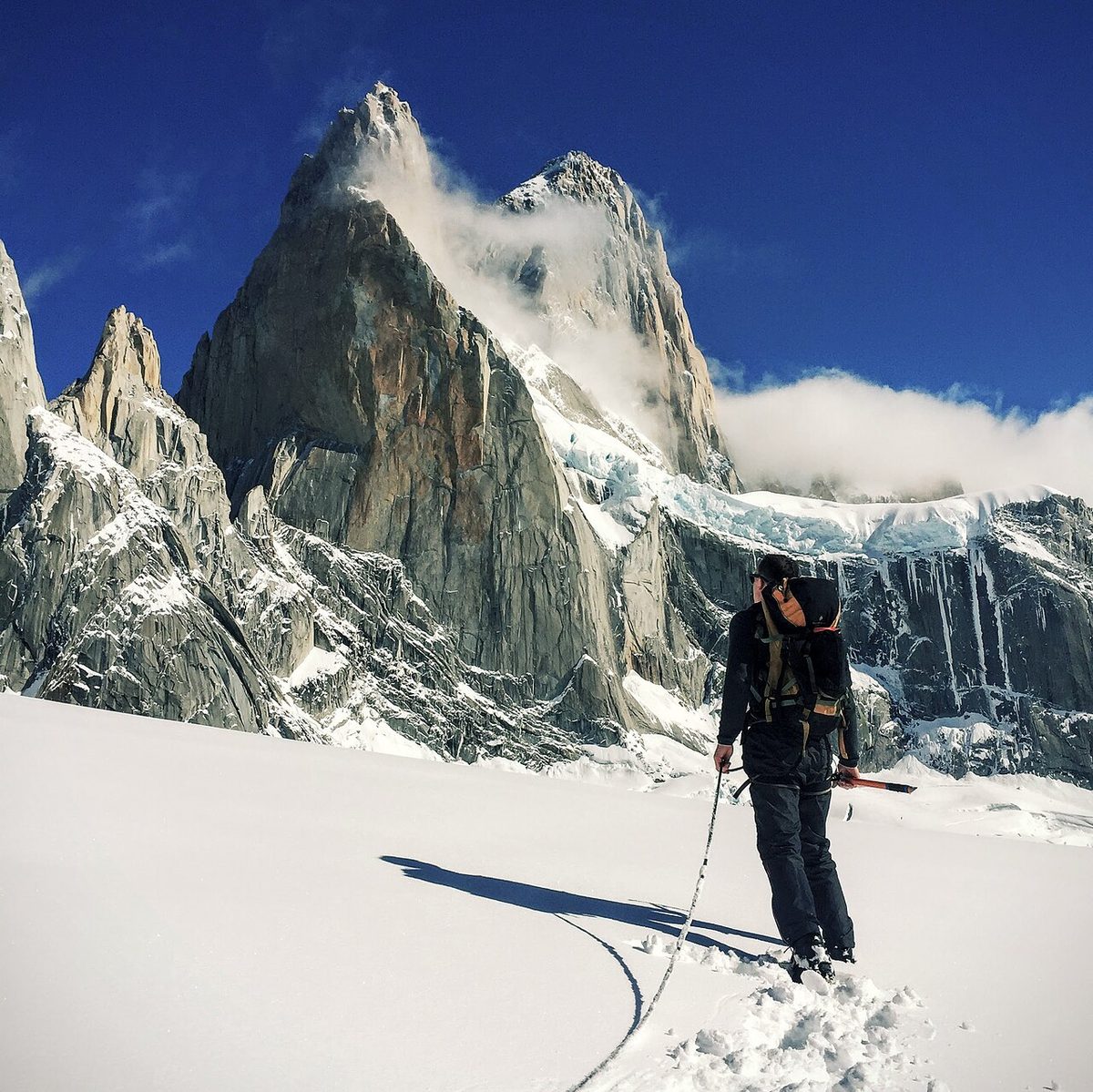 A hiker on snow below the granite spire of Fitz Roy near El Chaltén