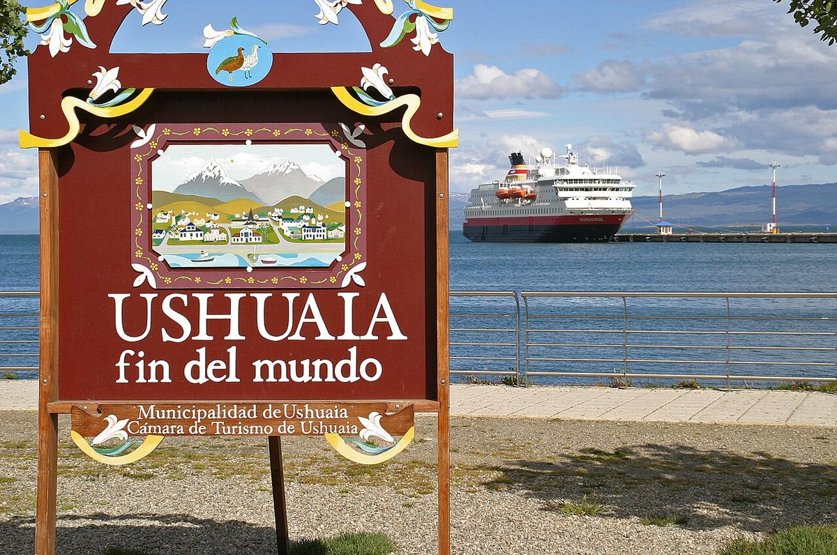 The Ushuaia fin del mundo sign on the downtown waterfront, with a cruise ship moored at the pier behind