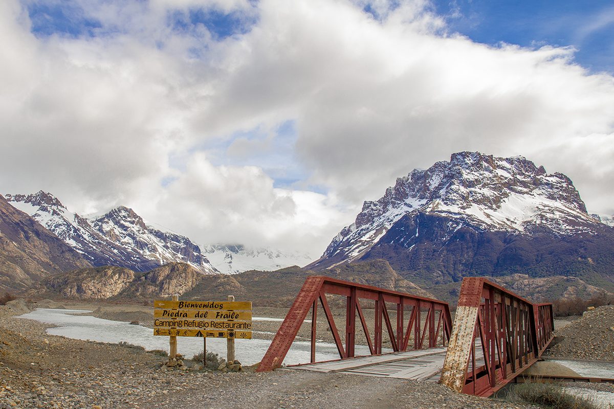 The bridge over the RÃo Eléctrico and the welcome sign for Piedra del Fraile, with snowy peaks behind