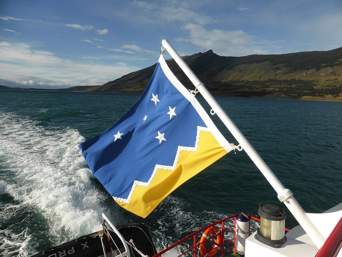 The Magallanes regional flag at the stern of a boat crossing the Última Esperanza fjord near Puerto Natales