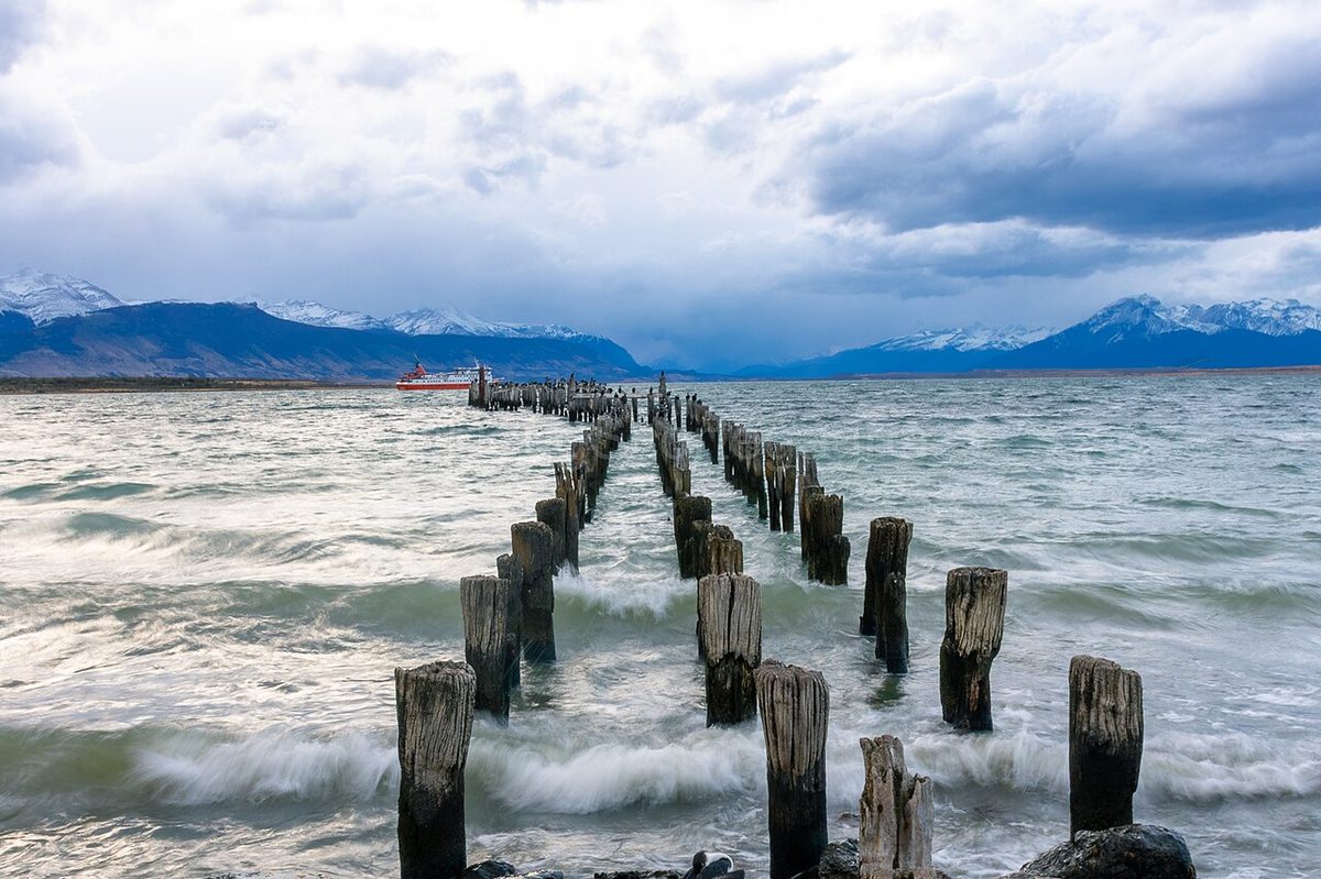 The old wooden pier pilings in the water off the Puerto Natales waterfront, with snowy mountains across the sound