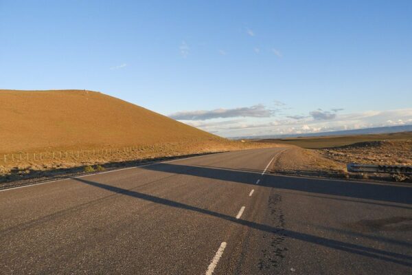Paved Ruta 40 sweeping past a bare, sunlit hillside on the Santa Cruz steppe