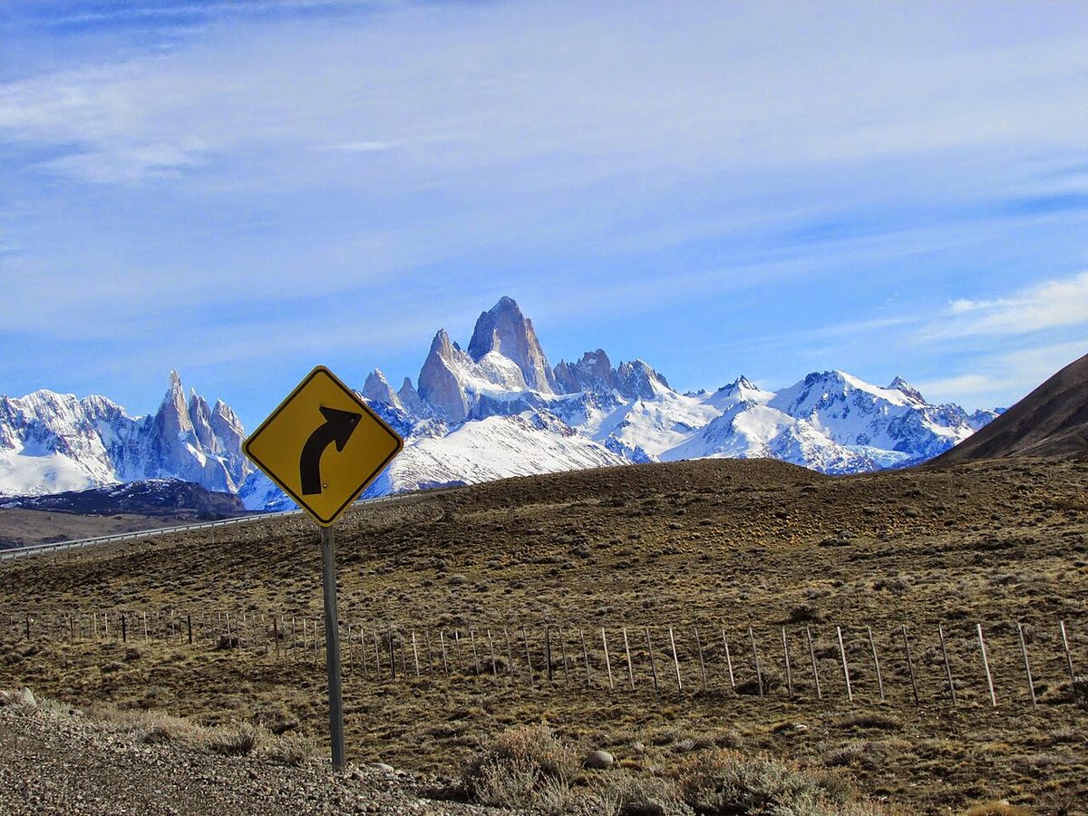A curve warning sign on the road to El Chaltén, with the snow-covered Fitz Roy massif behind