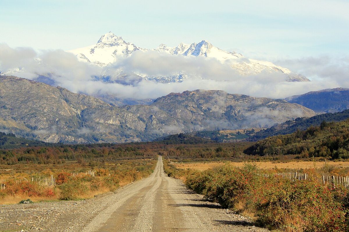 A gravel stretch of the Carretera Austral near the Leones valley in Aysén, with snow peaks rising behind