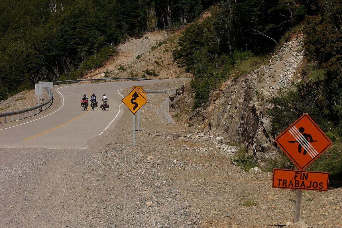 The point where asphalt gives way to a road-works section on the Carretera Austral, with cyclists climbing a mountain bend